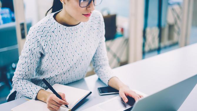 Woman with glasses looking at laptop with workbook